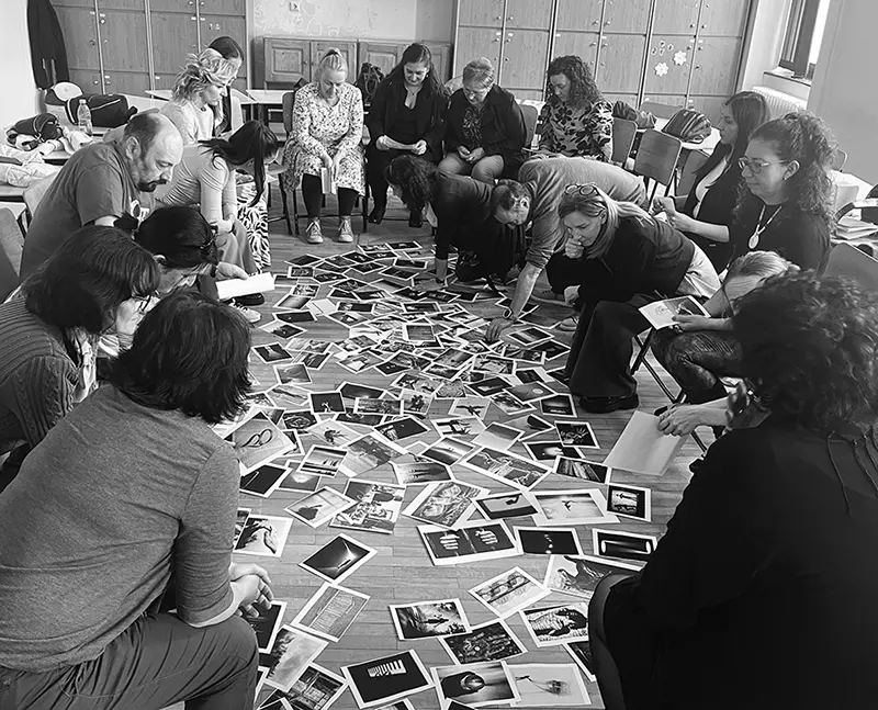 Csoportban ülő emberek, akik fényképeket néznek és beszélgetnek egy körben elrendezett térben.