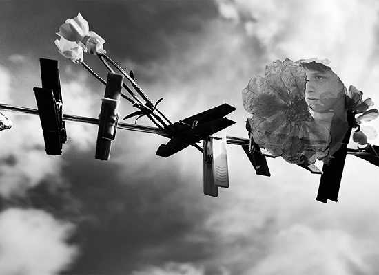 Fekete-fehér fotó ruhaszárító csipeszekről, virágokkal és egy arc részletével, felhős égbolt előtt